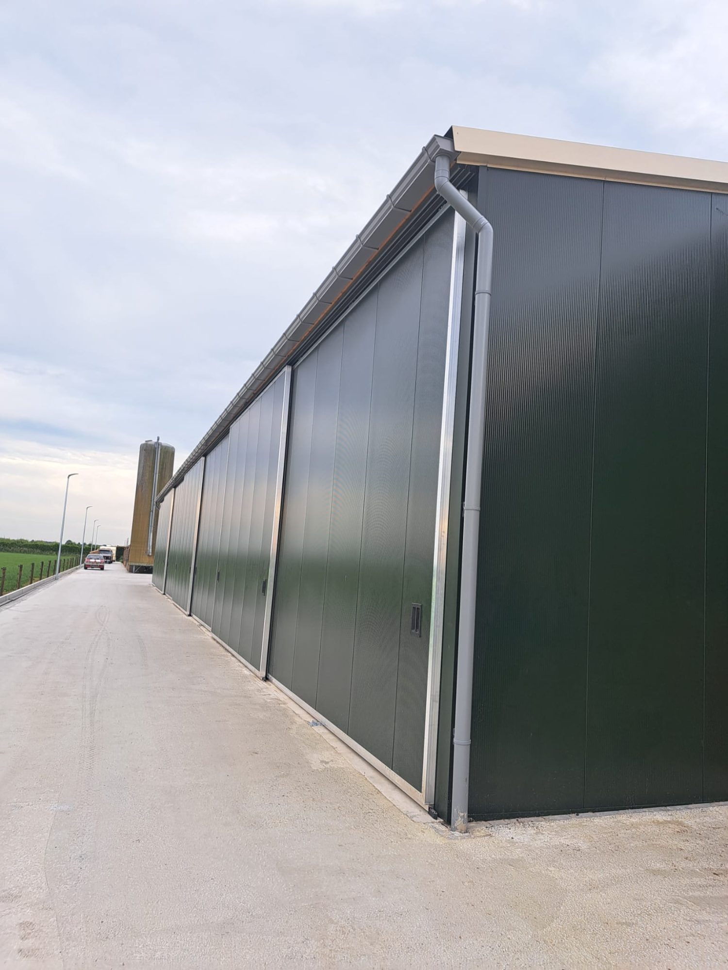 Aluminium dakgoot langs een taupe opslagloods met open vakken